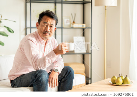 A senior man drinking coffee in the living room. 109276801