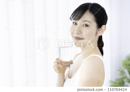 Woman drinking water in a bright room 110769424