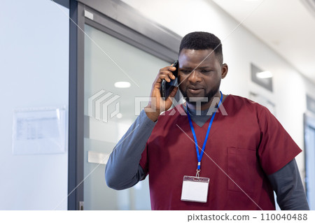 African american male doctor talking on smartphone in hospital corridor 110040488