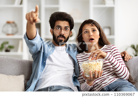 Shocked Young Indian Couple Watching Horror Movie On TV 110369067