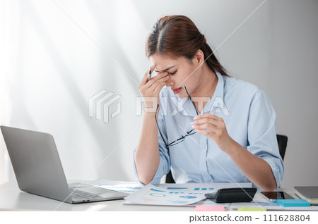 Stressed out Asian Business woman using calculator and laptop for doing math finance on an office desk, tax, report, accounting, statistics, and analytical research concept  111628804