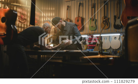 Two professional carpenters inspect wooden guitar body blank 111829279