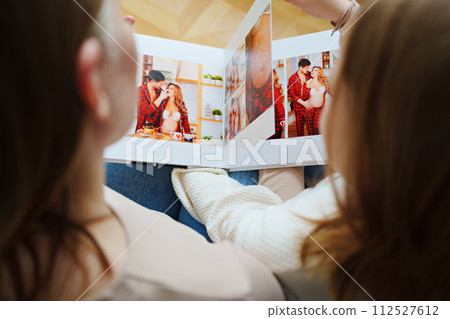 mother and daughter flips through a book with photos of dad and pregnant mom. 112527612