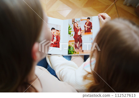 mother and daughter flips through a book with photos of dad and pregnant mom. 112527613