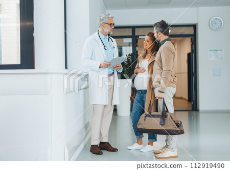 Pregnant woman and husband talking to obstetrician in hospital. Admitting woman in labor to maternity ward, planned cesarean section delivery. 112919490