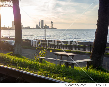 Seats with a table against the backdrop of the sea and the city. Nice place to eat. Sunset over the city. 112125311