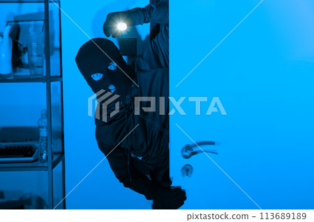 Burglar with flashlight opening a door stealthily 113689189