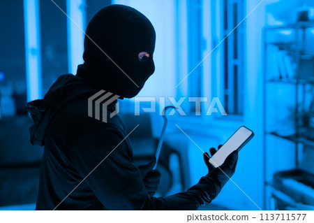 Thief using a smartphone during a break-in 113711577