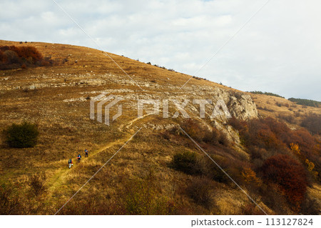 Group of three hikers going up the trail path. Wide shot of three backpackers climbing a mountans far from camera. Beautiful autumn scenery 113127824