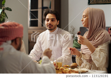 Over shoulder shot of young Muslim man talking to family members while having festive dinner on Uraza Bayram 113128191