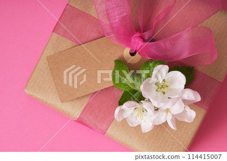 Brown craft gift box with empty tag, apple flowers on pink background. Place for your text 114415007