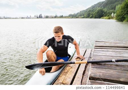 Canoeist man sitting in canoe holding paddle, getting out of water. Concept of canoeing as dynamic and adventurous sport. 114499841