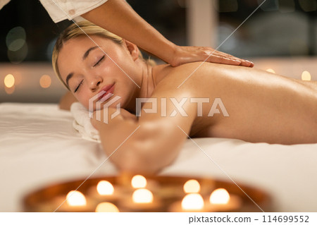 Captured in a serene spa, a young woman with blonde hair enjoys a soothing back massage, emphasizing relaxation and peacefulness. 114699552