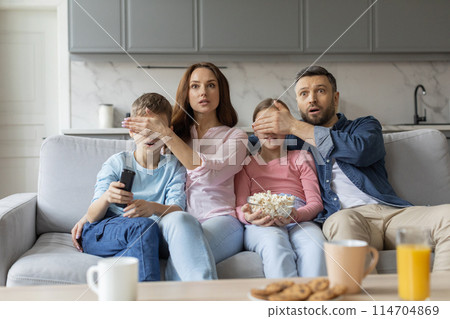 An astonished european family is bonded through love and shared experiences while watching a compelling scene on television, conveying affection and relationships in a home setting 114704869