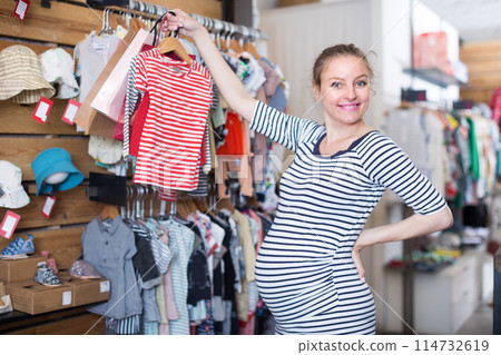 Pregnant woman in striped tunic chooses shirt in clothing shop 114732619