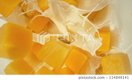 Fresh mango pieces falling into cream, top down view 114849141