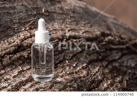 clear serum bottle with white dropper cap sits on weathered bark 114900740