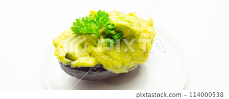 A green avocado with parsley on top sits on a white plate 114000538