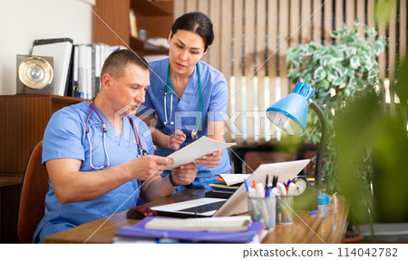 Two fellow doctors filling up medical forms on laptop in office 114042782