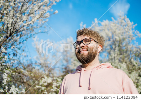 Male bearded man standing under branches with flowers of blooming almond or cherry tree in spring garden. Spring blossom. Copy space 114122084