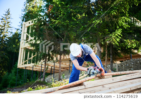 Carpenter using circular saw for cutting wooden plank. Man worker building wooden frame house. The ideology behind modern, environmentally-conscious construction. 114275619