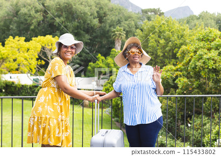 Senior African American woman and senior biracial woman greet warmly outdoors on vacation 115433802