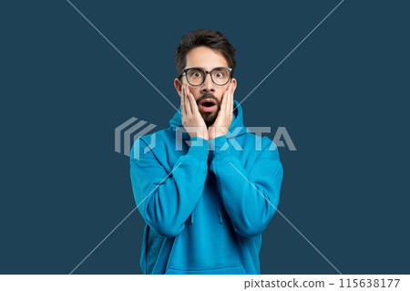 A man wearing a blue hoodie is covering his face with his hands in this candid street photograph. The mans expression is obscured, adding a sense of mystery to the scene. 115638177