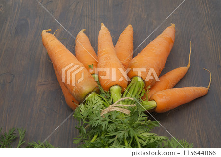 Bunch of bright orange carrots with lush green tops on rustic table 115644066