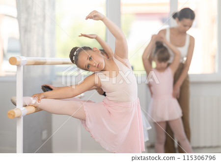 During group ballet class, girl put her foot on ballet bare and stretched her leg muscles. 115306796