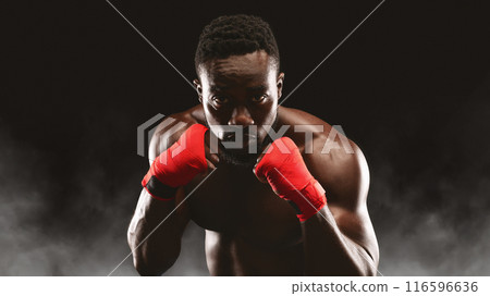 A close-up portrait of a boxer with his fists raised, ready to fight. 116596636