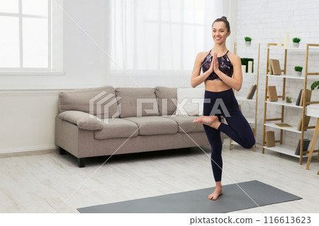 Tree pose. Young woman doing yoga, relaxing at home in living room, free space 116613623