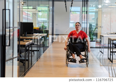 A modern young businesswoman in a wheelchair is surrounded by an inclusive workspace with glass-walled offices, embodying determination and innovation in the business world 116706725