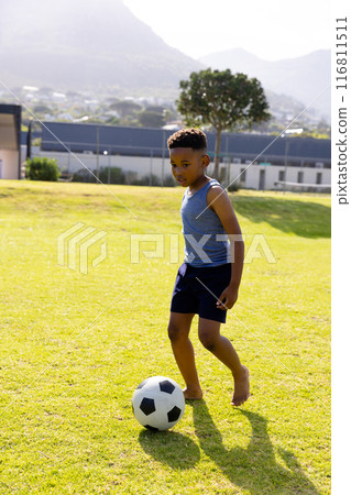 Happy african american schoolboy playing football on field at school 116811511