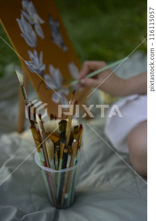 a beautiful young artist in a white dress paints a picture on the river bank 116115057