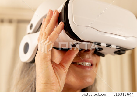 Using VR headset, mature woman exploring virtual reality at home 116315644