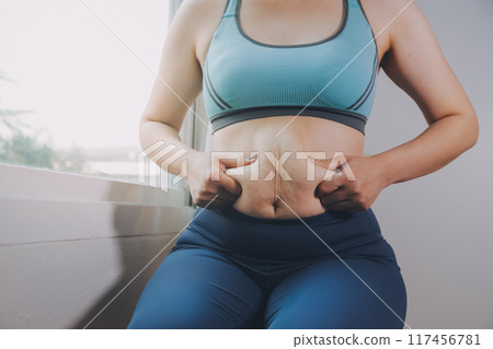 fat woman, fat belly, chubby, obese woman hand holding excessive belly fat with measure tape, woman diet lifestyle concept 117456781