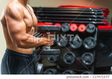 Upper body of an unrecognizable man lifting dumbbells in the gym 117471577