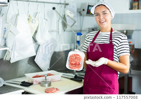 Female butcher demonstrating freshly formed beef hamburger patties 117557008