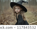 Young girl in a black witch costume wearing a pointed hat explores a forest during autumn in soft, natural lighting. Generative AI 117843532