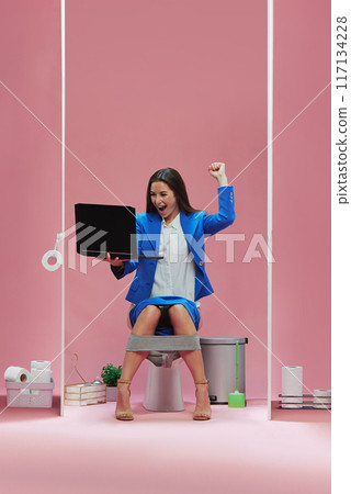 Goal. Emotional businesswoman sitting atop of toilet with laptop and watching live match event, cheering favorite soccer team against pink background 117134228