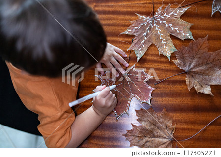 Child draws patterns on maple leaf with white gel pen. 117305271