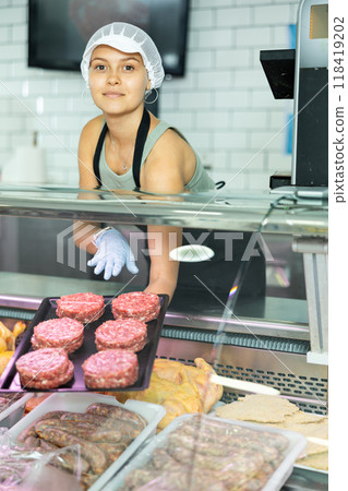 Saleswoman of butcher shop stands with tray and round blanks of ground beef, raw minced calf patties 118419202