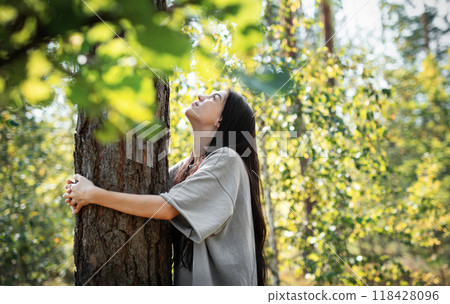 Young woman enjoying a peaceful moment by a tree in a lush green forest during daylight 118428096