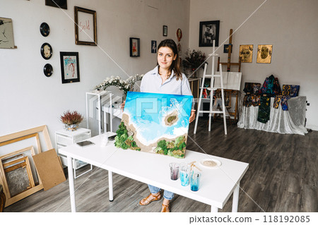 Female artist holding resin art coastal landscape, creative home studio, handmade beach scene, artistic workspace, DIY epoxy art, nature-inspired artwork, art creation process 118192085