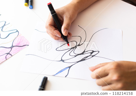 Hands drawing abstract lines with a black marker on white paper 118214158