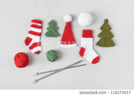 Knitted Christmas toys in form of red and white socks, Santa Claus hats, green Christmas trees with knitting balls and knitting needles on gray background. Top view, flat lay. 118273617