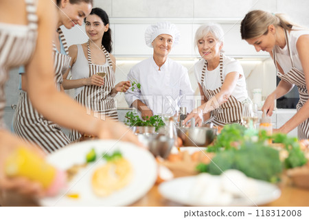 Mature female cook teaching members of cooking course over glass of wine 118312008