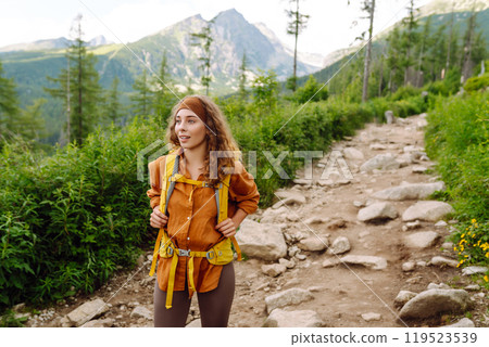 Woman traveler with yellow hiking backpack, hiking poles on trail among mountains. Adventure concept 119523539