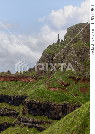 Layered basalt and red rock cliff at Giant's Causeway with columns lush greenery blue sky 119552901