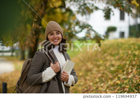 Female university student walking from a lecture to her dorm, passing through the autumn park. 119694937